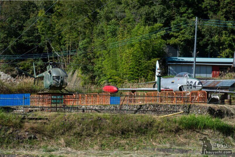空き地に展示されている「OH-6J（ヘリコプター）」と「T-33（練習機）」